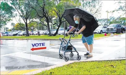  ?? Lynne Sladky The Associated Press ?? Franklin Castellon, 76, shields himself from the rain as he walks to an early voting site Monday in Miami.