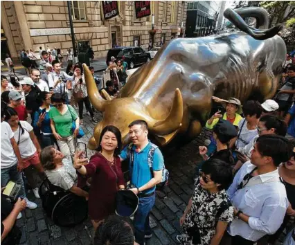  ?? Mark Lennihan / Associated Press ?? Tourists crowd around the Charging Bull statue in New York’s financial district to take photos. A debt-free vacation can be easy to accomplish with some careful planning.
