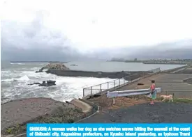  ?? — AFP ?? SHIBUSHI: A woman walks her dog as she watches waves hitting the seawall at the coast of Shibushi city, Kagoshima prefecture, on Kyushu Island yesterday, as typhoon Trami approaches.