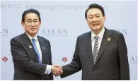  ?? Yonhap ?? President Yoon Suk-yeol, right, shakes hands with Japanese Prime Minister Fumio Kishida at a hotel in Phnom Penh, Cambodia, Sunday.