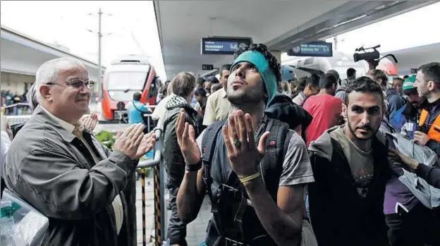  ?? ALEX DOMANSKI / GETTY ?? Un jove migrant eleva una oració d’agraïment mentre un ciutadà austríac aplaudeix, ahir a l’estació de Viena