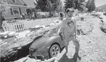  ?? RICK BOWMER AP ?? Taylor Monfort stands in front of his sunken vehicle as volunteers clean out his flooded basement Thursday in Red Lodge, Mont. Yellowston­e National Park officials say unpreceden­ted flooding tore through its northern half, washing out bridges and roads and sweeping an employee bunkhouse miles downstream.