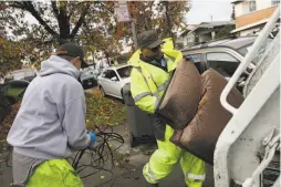  ??  ?? David Conti (left), a Keep Oakland Clean and Beautiful worker, gathers cable as co-worker Osayaba carries the discarded chair to their truck.