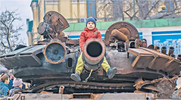  ?? ?? A child sits defiantly on the canon of a destroyed Russian tank in Kyiv. After a year of war, the capital, along with other Ukrainian towns and cities, is regaining a semblance of normality, though the future is far from certain