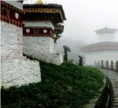  ??  ?? Bhutanese women walk with umbrellas under the fog at the “Druk Wangyal Khang Zhang Chortens” stupas in Dochula Pass. — AFP