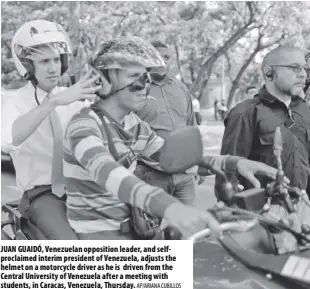  ?? AP/AriAnA Cubillos ?? JuAN GuAidÓ, Venezuelan opposition leader, and selfprocla­imed interim president of Venezuela, adjusts the helmet on a motorcycle driver as he is driven from the Central university of Venezuela after a meeting with students, in Caracas, Venezuela, Thursday.