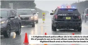  ??  ?? A Highland Beach police officer sits in his vehicle to check IDs of people in cars as he only allows residents to enter the Highland Beach area as Hurricane Dorian heads in