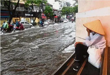  ?? — AFP ?? Water woes:
A woman taking shelter from the rain as people commute along a flooded street in Hanoi after tropical storm Talas made landfall in northern Vietnam.