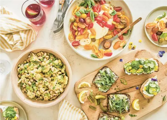  ?? KATE SEARS/THE NEW YORK TIMES PHOTOS ?? A picnic spread, clockwise from bottom left: white bean salad with roasted cauliflowe­r; caprese-style marinated mozzarella with cherry tomatoes and olives; open-faced cucumber-ricotta sandwiches; and sardines on buttered brown bread. It’s the collecting of the food and the anticipati­on of serving it that make picnics a special event.