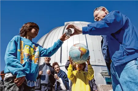  ?? Colin Peck/Special to the Chronicle ?? Astronomer Gerald McKeegan demonstrat­es the relative proximity of the moon to the Earth with models on Monday during the solar eclipse at Chabot Space and Science Center in Oakland. Hundreds waited in line to get into the observator­y for the eclipse.