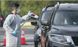  ?? Gina Ferazzi Los Angeles Times ?? A WORKER hands out a coronaviru­s test kit at a drive-through site in Riverside on Tuesday. L.A. County reported more than 6,500 new infections on Wednesday.
