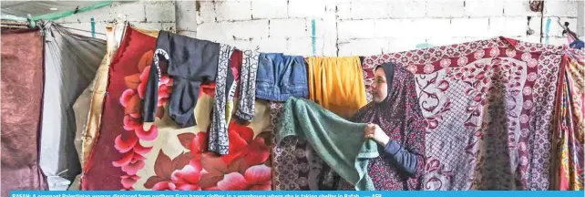  ?? — AFP ?? RAFAH: A pregnant Palestinia­n woman displaced from northern Gaza hangs clothes in a warehouse where she is taking shelter in Rafah.