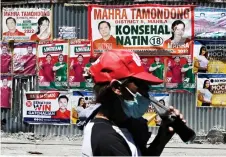  ?? — AFP photos ?? A man has a drink in front of posters plastered on a wall ahead of the May 9 presidenti­al election in Manila.