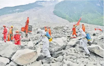  ??  ?? Epidemic prevention personnel (white suits) and rescue workers (orange suits) work at the site of a landslide in Xinmo village, Diexi town of Maoxian county, Sichuan province.— AFP photo