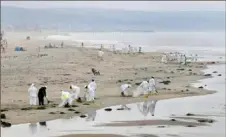  ?? Frederic J. Brown/AFP via Getty Images ?? A cleanup crew works on the beach Thursday in Newport Beach, Calif. Beaches normally thronged with the bronzed torsos of surfers are deserted as California races to clean up a huge oil spill.