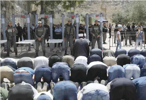  ?? — AFP ?? Muslim worshipper­s, who refuse to enter due to new security measures including metal detectors and cameras, pray as Israeli border policemen stand outside the Lion’s Gate, a main entrance to Al Aqsa mosque compound, in Jerusalem’s Old City, on Sunday...