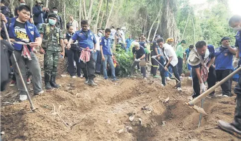  ??  ?? This file picture shows rescue workers and forensic officials digging out skeletons from shallow graves covered by bamboo at the site of a mass grave at an abandoned jungle camp in the Sadao district of Thailand’s southern Songkhla province bordering...