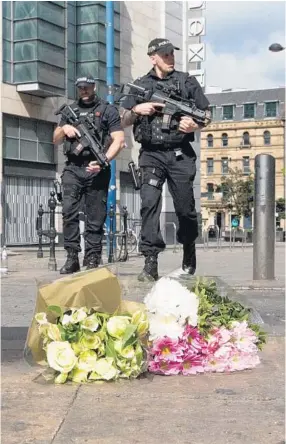  ?? CHRISTOPHE­R FURLONG/GETTY IMAGES ?? Police in Manchester, England patrol past floral tributes to the victims of the terrorist attack. An explosion occurred at Manchester Arena as concertgoe­rs were leaving the venue after Ariana Grande had performed. Britain raised its terror-threat level...