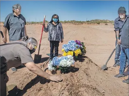  ?? Photograph­s by Brian van der Brug Los Angeles Times ?? CARLITA BERGEN, center, holds a shovel as Officer Carolyn Tallsalt smooths dirt over the grave of Arnold Billy, who died of COVID-19, at his funeral in Tuba City. Looking on are mortuary officiant Robert Dayzie, left, and Arnold’s brother Ronald Billy.