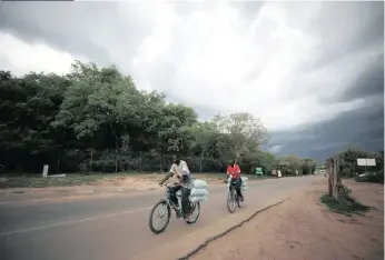  ??  ?? STORM clouds gather as cyclists return with goods from the Zambian border at Victoria Falls, Zimbabwe.| Reuters