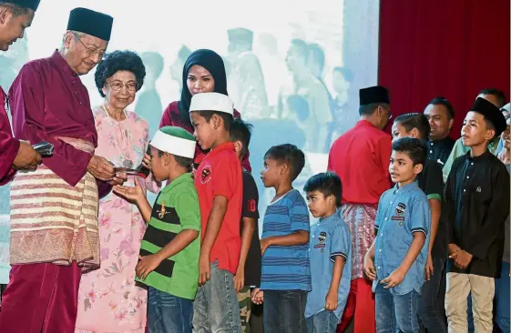  ?? — Bernama ?? Sharing the joy: Dr Mahathir presenting duit raya to children at his Hari Raya open house at Lada Sports Complex in Kuah, Langkawi. With him is Tun Dr Siti Hasmah Mohamad Ali.
