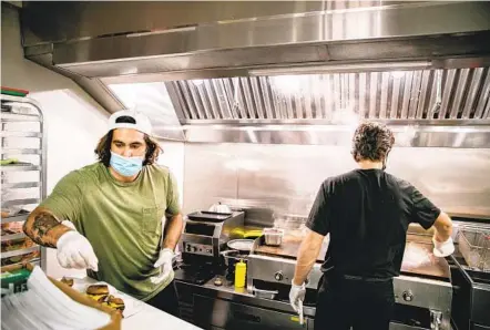  ?? SAM HODGSON U-T ?? Alejandro Ballestero­s and Jose Honold, part-owners of Hayes Burger, cook burgers inside the restaurant's kitchen in Barrio Logan on Wednesday. After years of trying to open, the owners finally got their permits this year and opened in April, in the midst of the pandemic.