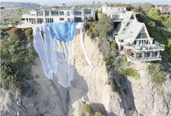  ?? MARIO TAMA /GETTY IMAGES NORTH AMERICA/GETTY IMAGES VIA AGENCE FRANCE-PRESSE ?? AERIAL view of mansions still standing along a cliff after a portion of the cliffside tumbled to the Pacific Ocean following days of heavy rains earlier this month in Dana Point, California. Tons of cliffside rocks and dirt fell to the beach below during the landslide but authoritie­s say there is no imminent threat to the homes.