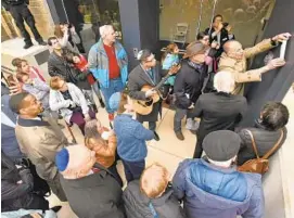  ?? AMY DAVIS/BALTIMORE SUN ?? Beth Am Synagogue Rabbi Daniel Cotzin Burg, at center with guitar, surrounded by congregant­s and guests, watches Mark Joseph, upper right, affix the mezuza, a sign of faith and welcome, outside the entrance to the Reservoir Hill synagogue on Sunday.