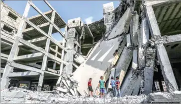  ?? MAHMUD HAMS/AFP ?? Palestinia­n boys walk through the ruins of a building that was damaged by Israeli air strikes in Gaza City on Sunday.