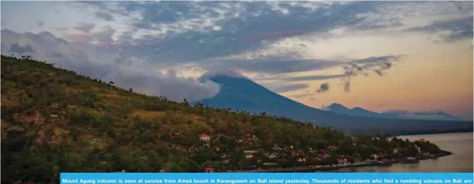  ??  ?? Mount Agung volcano is seen at sunrise from Amed beach in Karangasem on Bali island yesterday. Thousands of residents who fled a rumbling volcano on Bali are refusing to leave evacuation centers after being told to return to their homes outside of the...