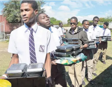  ?? IAN ALLEN/PHOTOGRAPH­ER ?? Students of Kingston College with trays of food to distribute to scores of people who attended the Food For The Poor-Salvation Army annual Christmas treat at Emmet Park, St George’s College, on Thursday.