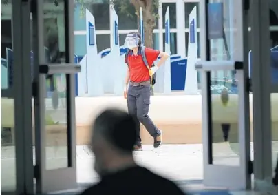  ?? AMY BETH BENNETT/SOUTH FLORIDA SUN SENTINEL ?? A man walks across campus wearing a mask, face shield and gloves at Nova Southeaste­rn University’s Davie campus on Aug. 20.