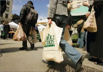  ?? THE ASSOCIATED PRESS ?? A shopper at the Greenmarke­t at Union Square walks through the market carrying a bag of groceries from the Whole Foods grocery store on the other side of the square in New York. Online juggernaut Amazon announced Friday that it is buying Whole Foods in...