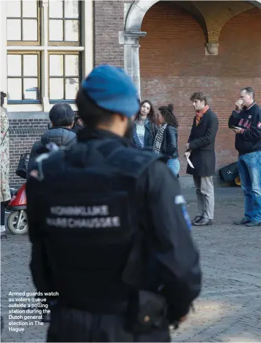  ??  ?? Armed guards watch as voters queue outside a polling station during the Dutch general election in The Hague