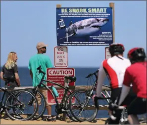  ?? (File Photo/AP/Charles Krupa) ?? A couple stands next to a shark warning sign May 22, 2019, while looking at the ocean at Lecount Hollow Beach in Wellfleet, Mass.