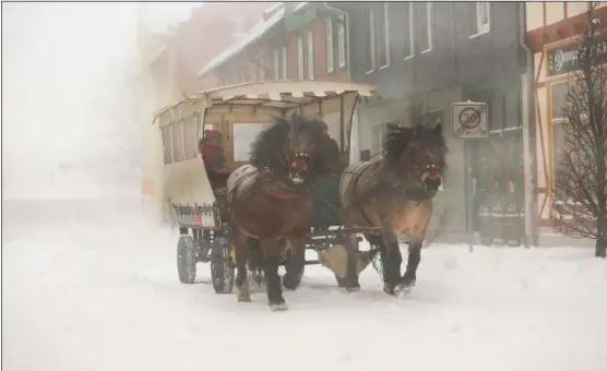  ?? (AP/Matthias Bein) ?? A horse-drawn carriage drives through the town in the snow flurry in Wernigerod­e, Germany, on Sunday.