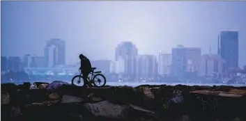  ?? ALLEN J. SCHABEN Los Angeles Times ?? THE NUMBER of unsheltere­d individual­s increased dramatical­ly in Long Beach during the pandemic. Above, a person walks their bike on the Alamitos Bay jetty with the Long Beach skyline in the background.