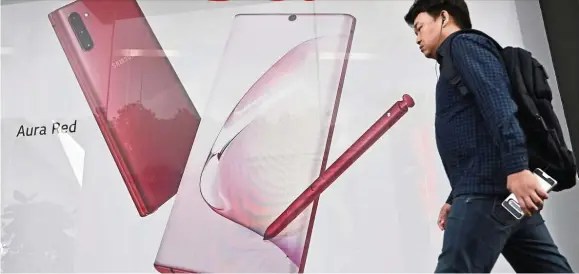  ?? — AFP ?? in Seoul. Samsung Electronic­s expects a Powered by 5G: A man walking past an advertisem­ent for the Samsung Galaxy Note 10 5G smartphone smaller-than-expected fall in third quarter operating profit due to strong sales of the Note 10.