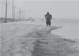  ??  ?? ■ LEFT: An Omani man walks on the road covered by the floodwater after Cyclone Merkunu on Saturday in Salalah, Oman.