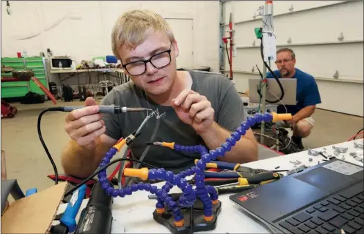  ??  ?? Nicholas Moehring, an electrical engineerin­g intern from Wichita State University, solders July 6 while creating a wire harness for robots as Andy Helten, senior engineer, works on a robot in the Greenfield Robotics shop near Cheney, Kan.
(AP/Sandra J. Milburn/The Hutchinson News)