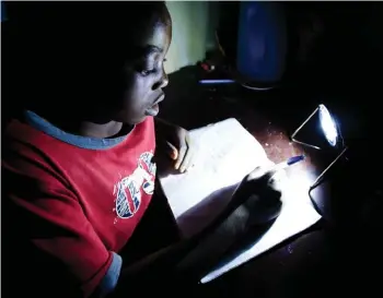  ??  ?? Below: A student in Zambia uses a solar-powered lamp from Solar Aid