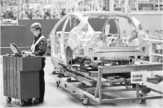  ??  ?? An employee uses a laptop next to a car body at an assembly line at a Ford manufactur­ing plant in Chongqing municipali­ty. Ford Motor Co said it will move some production of its Focus small car to China and import the vehicles to the United States in a...