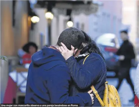  ??  ?? Una mujer con mascarilla observa a una pareja besándose en Roma.