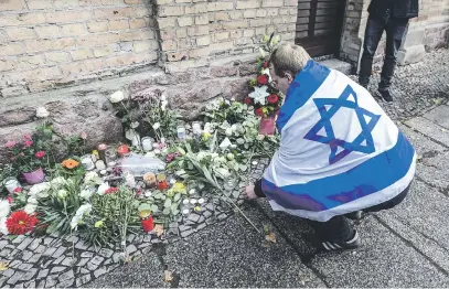  ?? Picture: EPA-EFE ?? LAST RESPECTS. A man draped in an Israel flag lays flowers in front of the synagogue in Halle Saale, Germany, yesterday, after two people were killed and two injured during a shooting on Wednesday.