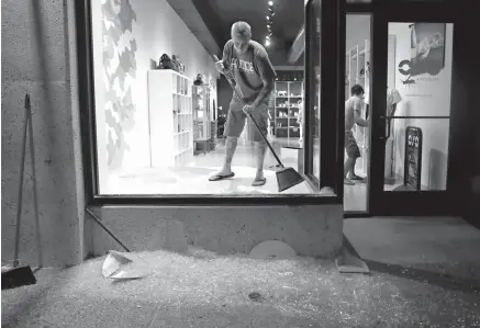  ?? Associated Press ?? n Scott McRoberts helps clean up broken glass after a violent crowd broke windows on many businesses after clashing with police Saturday in University City, Mo. Earlier, protesters marched peacefully in response to a not-guilty verdict in the trial of...