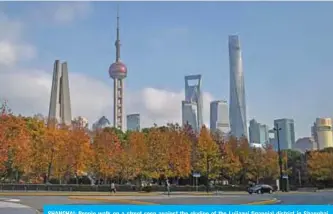  ?? — AFP ?? SHANGHAI: People walk on a street seen against the skyline of the Lujiazui financial district in Shanghai yesterday.