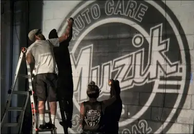  ?? PHOTOS BY RICHARD PAYERCHIN — THE MORNING JOURNAL ?? Mural artist Mike Sekletar and partner Val Fiehl trace the outline of a new retro-inspired logo for Muzik’s Auto Care on Aug. 23 on the back wall of the garage at 704 W. Erie Ave. Painting began a day later and will continue as weather permits, said shop owner John Muzik, who commission­ed the artwork.