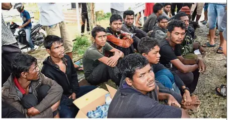  ??  ?? Long way from home: Men believed to be Rohingyas sitting on the ground after arriving in East Aceh. — AFP