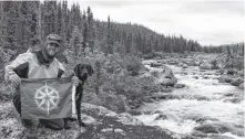  ?? SUBMITTED ?? The waters of the Red Wine River in Labrador served as a backdrop for this photo as Justin Barbour and his trusty guide Saku pose along with his Newfoundla­nd Explorer flag.