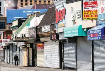  ?? Associated Press ?? A person wearing a protective face mask as a precaution against the coronaviru­s walks past shuttered businesses on the boardwalk in Atlantic City, N.J.